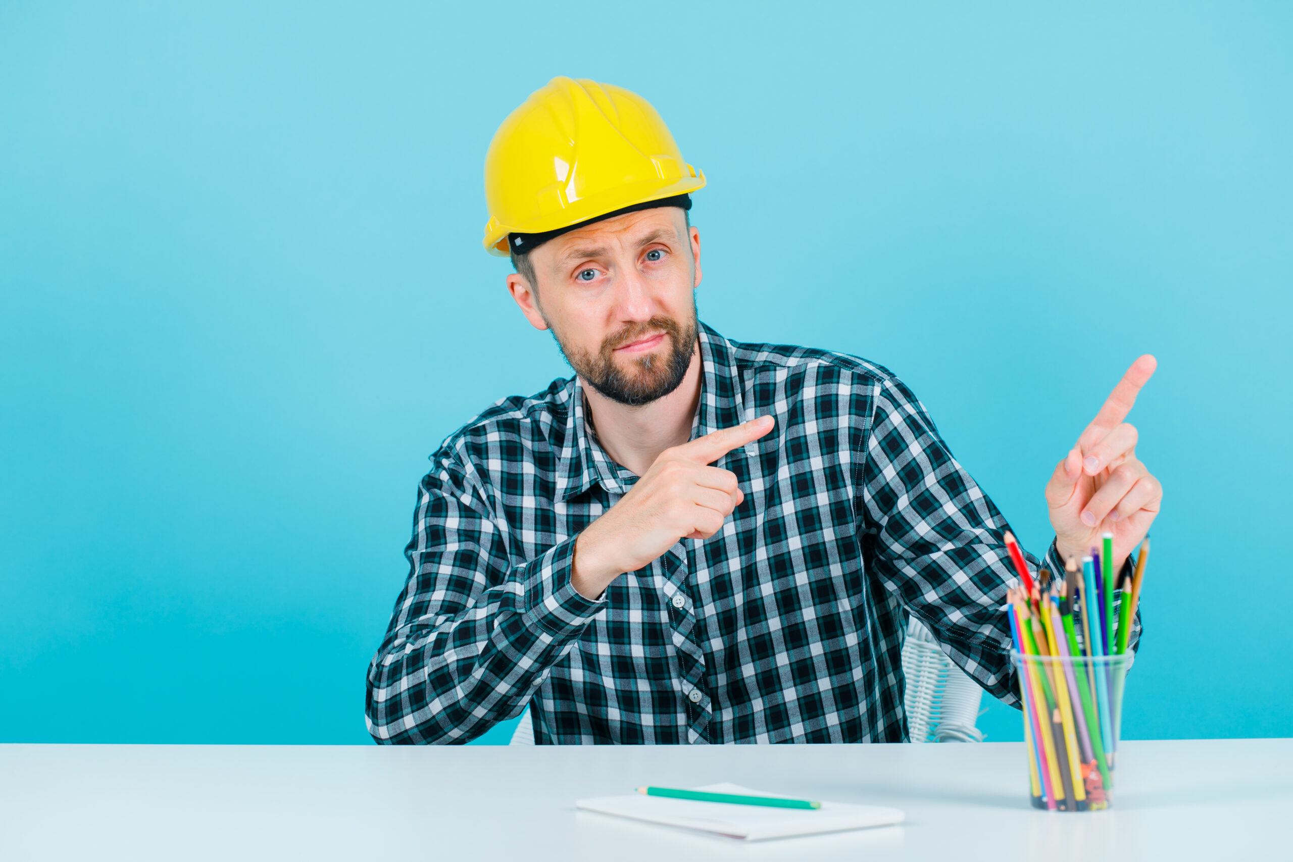 Young engineer man is pointing right with forefingers on blue background